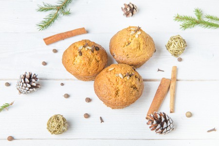 Christmas composition. Christmas cupcakes with spices cloves, seeds and nuts, notepad, pen, pine cones on wooden white background. Flat lay, top view.の写真素材