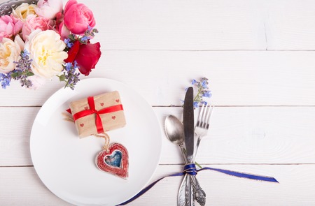 Festive table setting for Valentine's Day with fork, knife, hearts and bouquet of English rose on a white wooden table. Top view.の写真素材