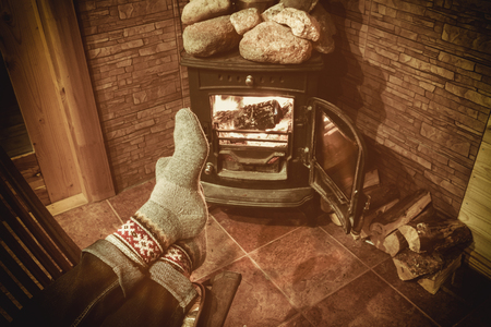 Feet in woolen socks by the Christmas fireplace. Man relaxes by warm fire with a cup of hot drink and warming up her feet in woolen socks.の写真素材