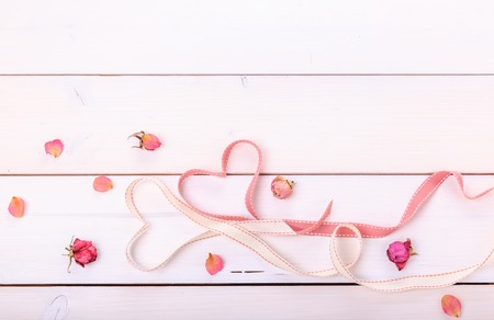 Two ribbon magic pink hearts on white wooden backround, roses and petals. Valentine day conceptの写真素材