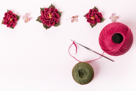 Roll the cotton purple and green yarn and crochet hook, crocheted rose flowers, decoration, ornament, brooch on white background. The concept of crochet hobby, needlework, self-realization, creativityの写真素材
