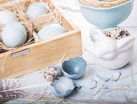 Easter decoration with dyed blue eggs and sawed eggs, feathers in a wooden box, festive background,...