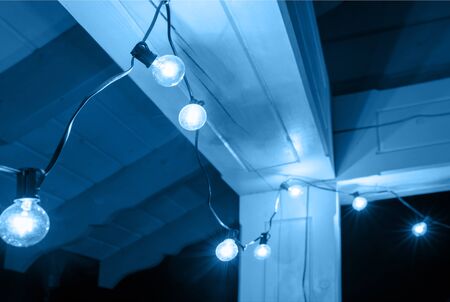 Decorative street lights hanging on the terrace of a wooden house at night. Old decorative lamps, festive lighting. Thunderstorm clouds sky background. Color of the year 2020 classic blueの写真素材