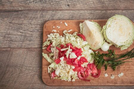 Fresh organic vegetables, chopped cabbage and tomatoes, greens, dill, parsley on a wooden board and a rustic table, place for an inscriptionの写真素材