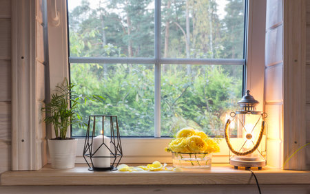 Autumn bouquet of yellow roses on the windowsill, candles, flowers, lantern. Scandinavian style. White window with mosquito net in rustic wooden houseの写真素材
