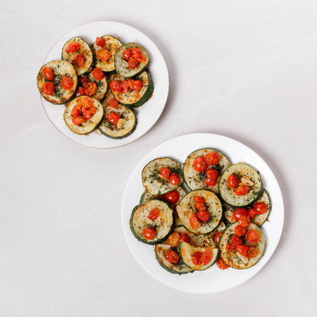 Fried zucchini with garlic and cherry tomatoes on white plate and grey marble table.の写真素材