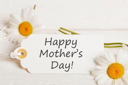 White composition for Mothers Day with white flowers daisies and card featuring heartfelt text Happy Mothers Day. theme highlighted by gentle light, emphasizing love through text and white eleganceの写真素材