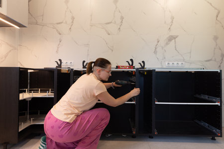 Woman assembling kitchen cabinet with power drill, installing drawer runners, modern marble backsplash, step-by-step DIY renovation, real home improvement, female builder, interior updateの写真素材