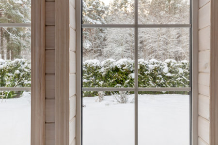 Winter view through large window, snowy forest, cozy wooden interior, calm seasonal mood, soft...
