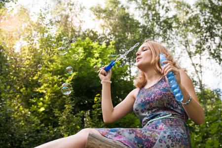 Young girl sitting on a tree in a park playing with soap bubblesの写真素材