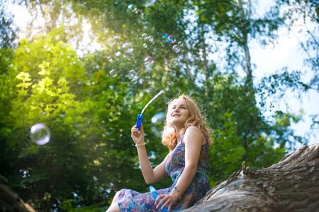 Young girl sitting on a tree in a park playing with soap bubbles