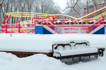 GOMEL, BELARUS - JANUARY 12, 2017: Snowy attraction "Funny roller coaster" and bench in winter park during snowfall, Gomel, Belarusのeditorial素材