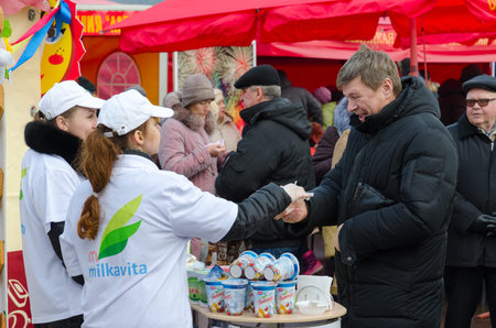 GOMEL, BELARUS - FEBRUARY 21, 2015: Young girls-sellers offer tasting of dairy products at fair during mass Shrovetide festivitiesのeditorial素材