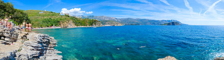 BUDVA, MONTENEGRO - SEPTEMBER 7, 2017: Unknown people admire panoramic view of Budva coast (Mogren beach, Budva Old Town, Sveti Nikola Island) from high cliff near beach, Montenegroのeditorial素材