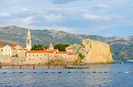 BUDVA, MONTENEGRO - SEPTEMBER 5, 2017: Unknown tourists rest on beach near walls of Old Town in popular resort city of Budva, Montenegroのeditorial素材