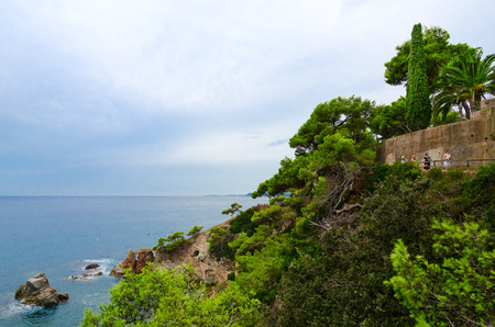 LLORET DE MAR, SPAIN - SEPTEMBER 10, 2018: Unidentified tourists walk along walking path along beautiful rocky coast in popular resort town of Lloret de Mar, Costa Brava, Catalonia, Spainのeditorial素材