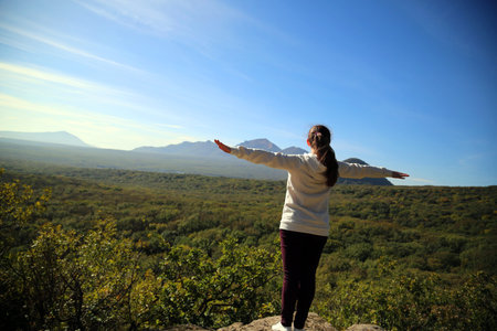A young woman stands on top of a mountain on a large stone.