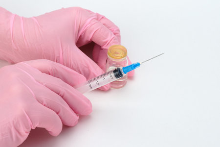 A doctor in medical gloves holds a syringe and a vial with a vaccine or drug in his hands.