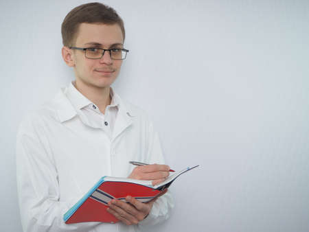Portrait of a young man of European appearance in a white medical coat. A young doctor in a white coat. Medical student. . High quality photoの写真素材