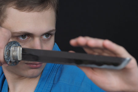 Portrait of a young man in a blue kimono with a sword. Black background. High quality photoの写真素材