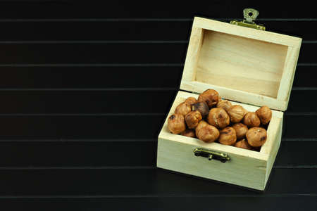 Nuts, hazelnuts peeled in a wooden box. Hazelnut kernels in a wooden chest, close-up on a black background.の写真素材