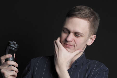 Shave safely. A young man or man of European appearance shaves his face with an electric razor. High quality photoの写真素材