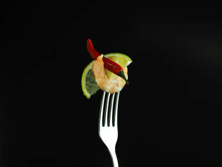 Shrimp with lime and red pepper on a fork. Seafood snack on a black background. High quality photoの写真素材