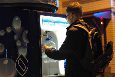 A person collects clean drinking water into a poastic bottle from a device installed on the street....