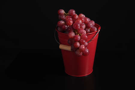 Still life, a bunch of red large grapes in a red bucket on a black background. ... High quality photoの写真素材