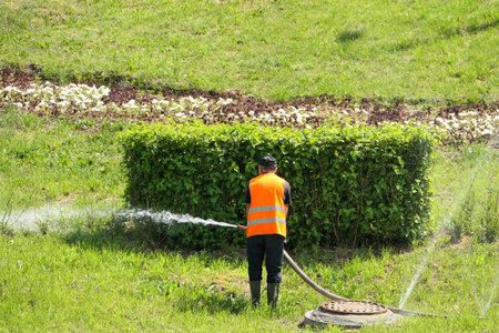 A man waters lawns and flower beds with a watering machine in summer in the city in hot weather.. High quality photoの写真素材