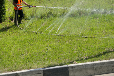 A man waters lawns and flower beds with a watering machine in summer in the city in hot weather.....
