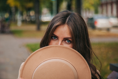 girl with hat in hand sitting on a bench in a city parkの写真素材
