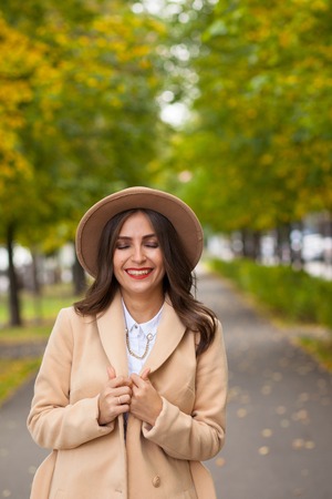 Portrait of a girl walking along the alley in a coat, a hat on a background of autumn treesの写真素材