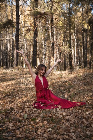girl in red dress throwing leaves in the forestの写真素材