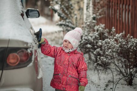 little girl brushing snow off the car brushの写真素材