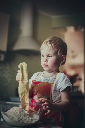 little girl baking cookies. Pour the flour into the cupの写真素材