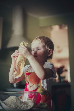 little girl baking cookies. Pour the flour into the cupの写真素材