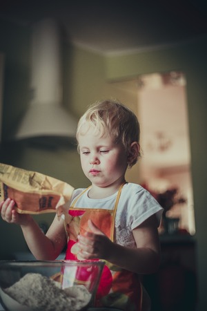 little girl baking cookies. Pour the flour into the cupの写真素材