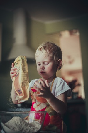 little girl baking cookies. Pour the flour into the cupの写真素材