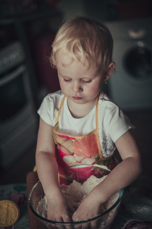 little girl baking cookies. Flour stirred in a cup of her handsの写真素材