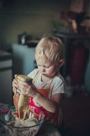 little girl baking cookies. Pour the flour into the cupの写真素材