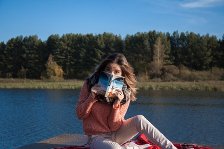 Beautiful girl with book sits on the shore of the lakeの写真素材