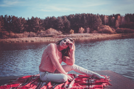 Beautiful girl with book sits on the shore of the lakeの写真素材