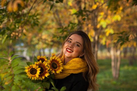 Beautiful girl with sunflowers in the autumn rowanの写真素材
