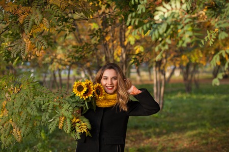 Beautiful girl with sunflowers in the autumn rowanの写真素材