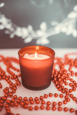 Red Christmas candle and Christmas beads on a black background with a wreath