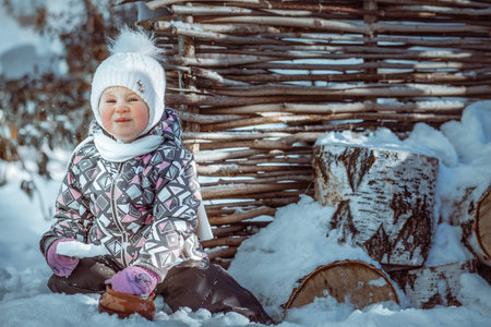 baby sitting on a stump in snow with a pot in the hands of