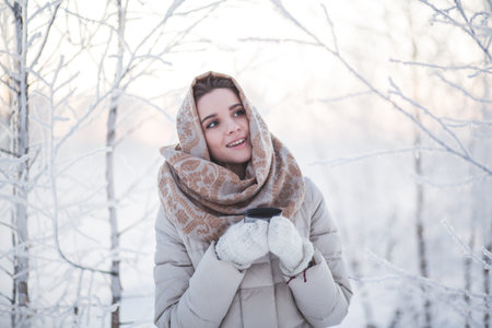 winter portrait of a girl in a winter forest at sunset. drinks hot teaの写真素材