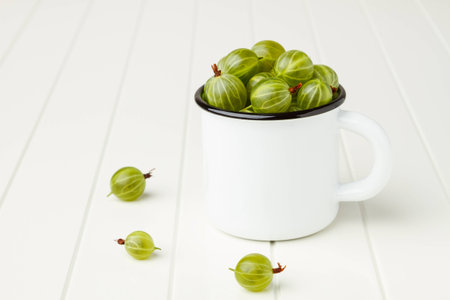 Fresh green gooseberries in an enamel mug on white tableの写真素材