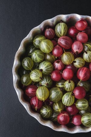 Gooseberries in a metal baking pan on a black background. Top viewの写真素材